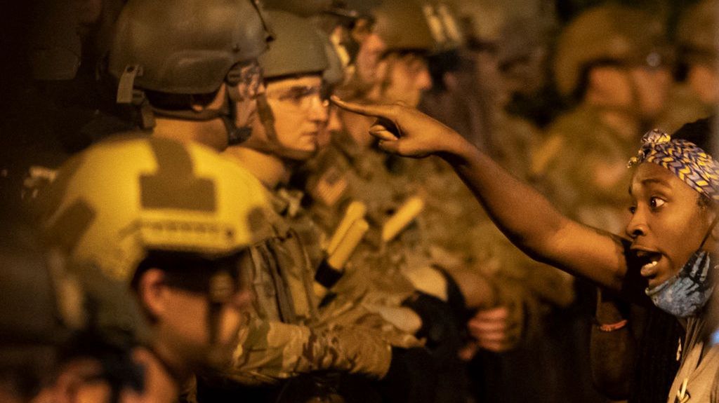 Protestująca kobieta przed szpalerem policjantów pilnujących Białego Domu